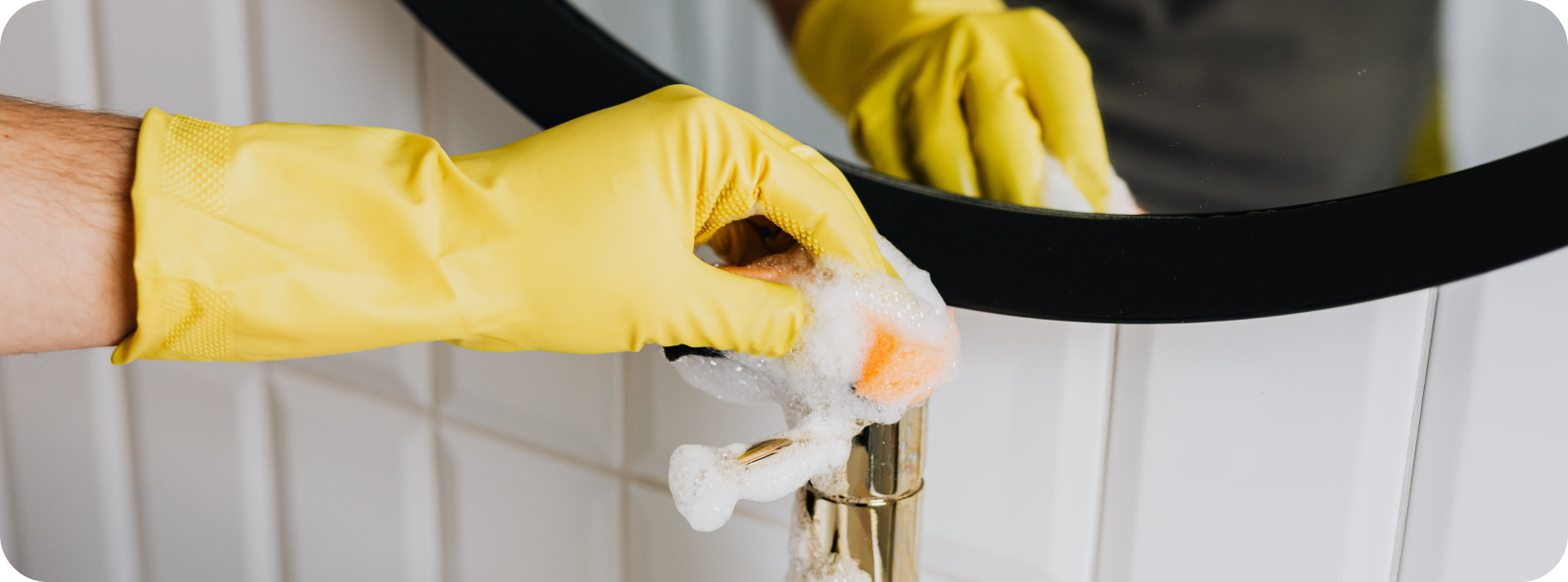 hand with yellow glove wiping bathroom sink