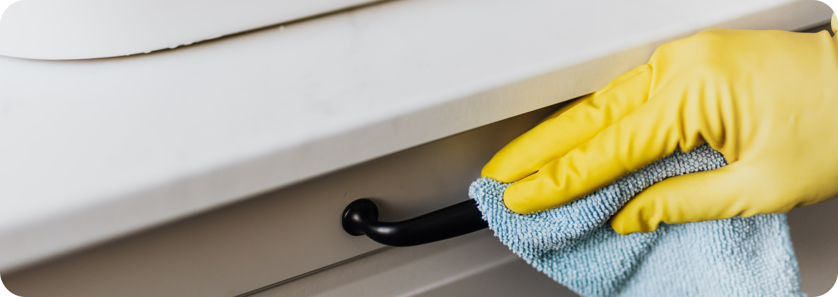 hand with yellow glove wiping down wardrobe drawer with blue cloth